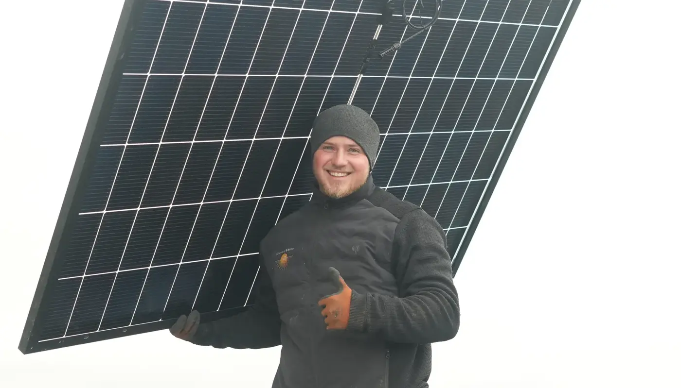 Monteur von Sonne & Wärme trägt ein Solarmodul über das Dach