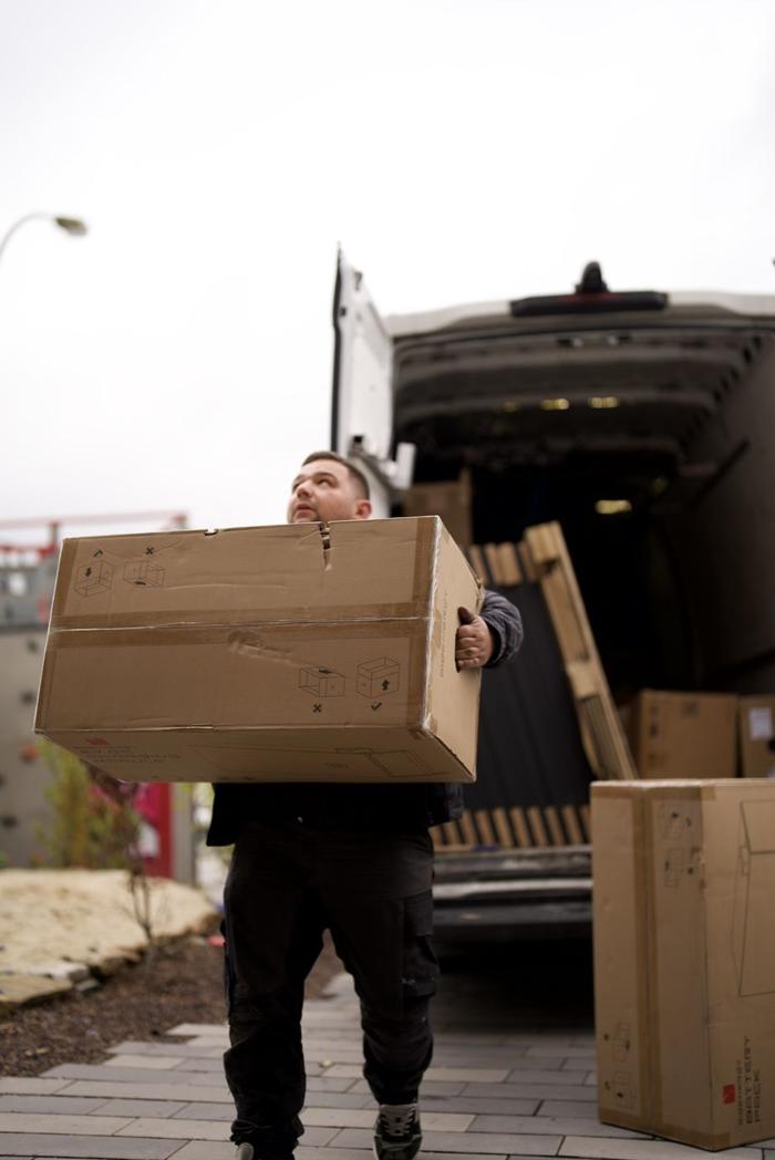 Monteur trägt einen Materialkarton aus dem Transporter