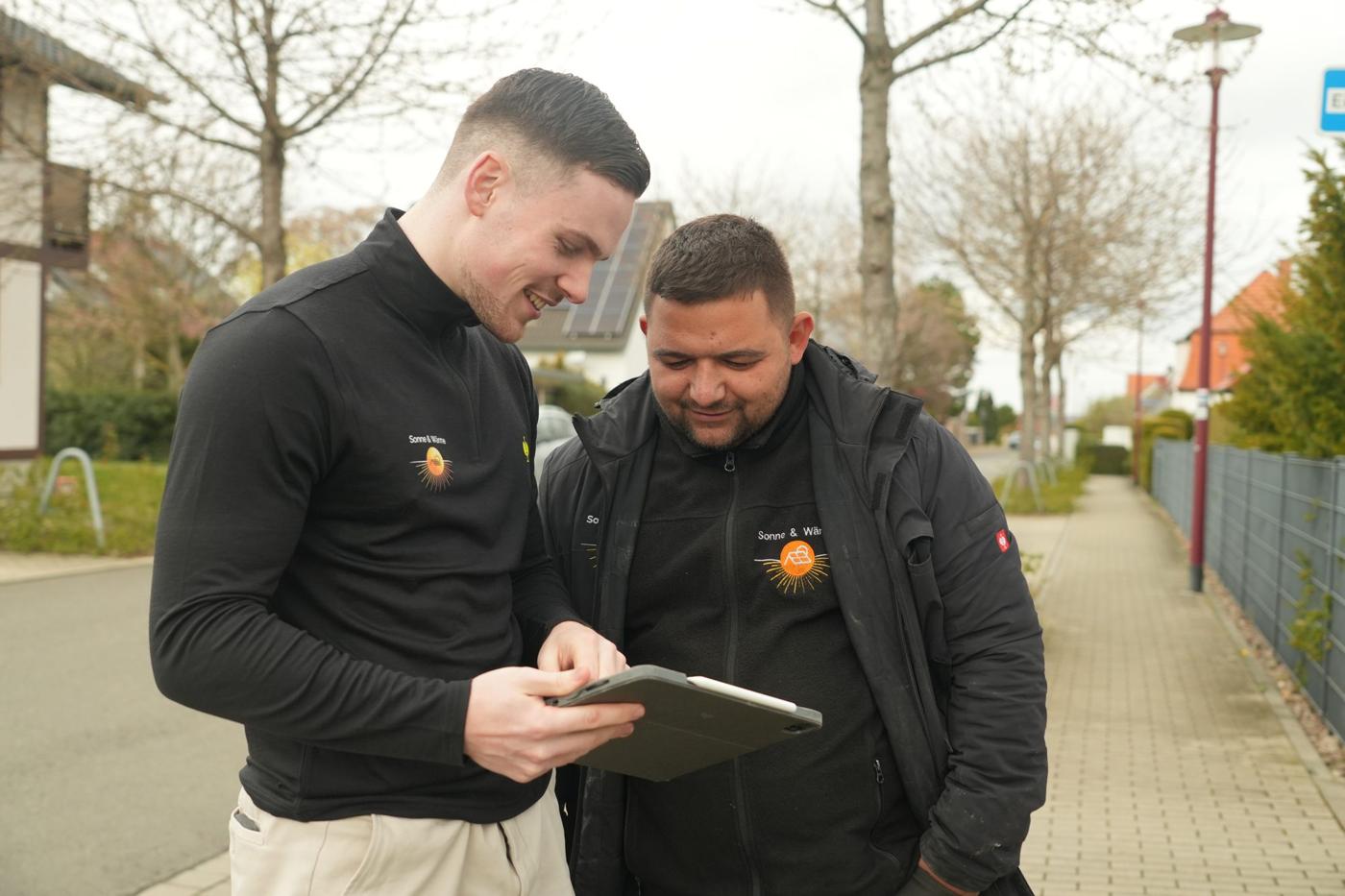 Zwei Mitarbeiter von Sonne & Wärme besprechen lachend ein Projekt am Tablet
