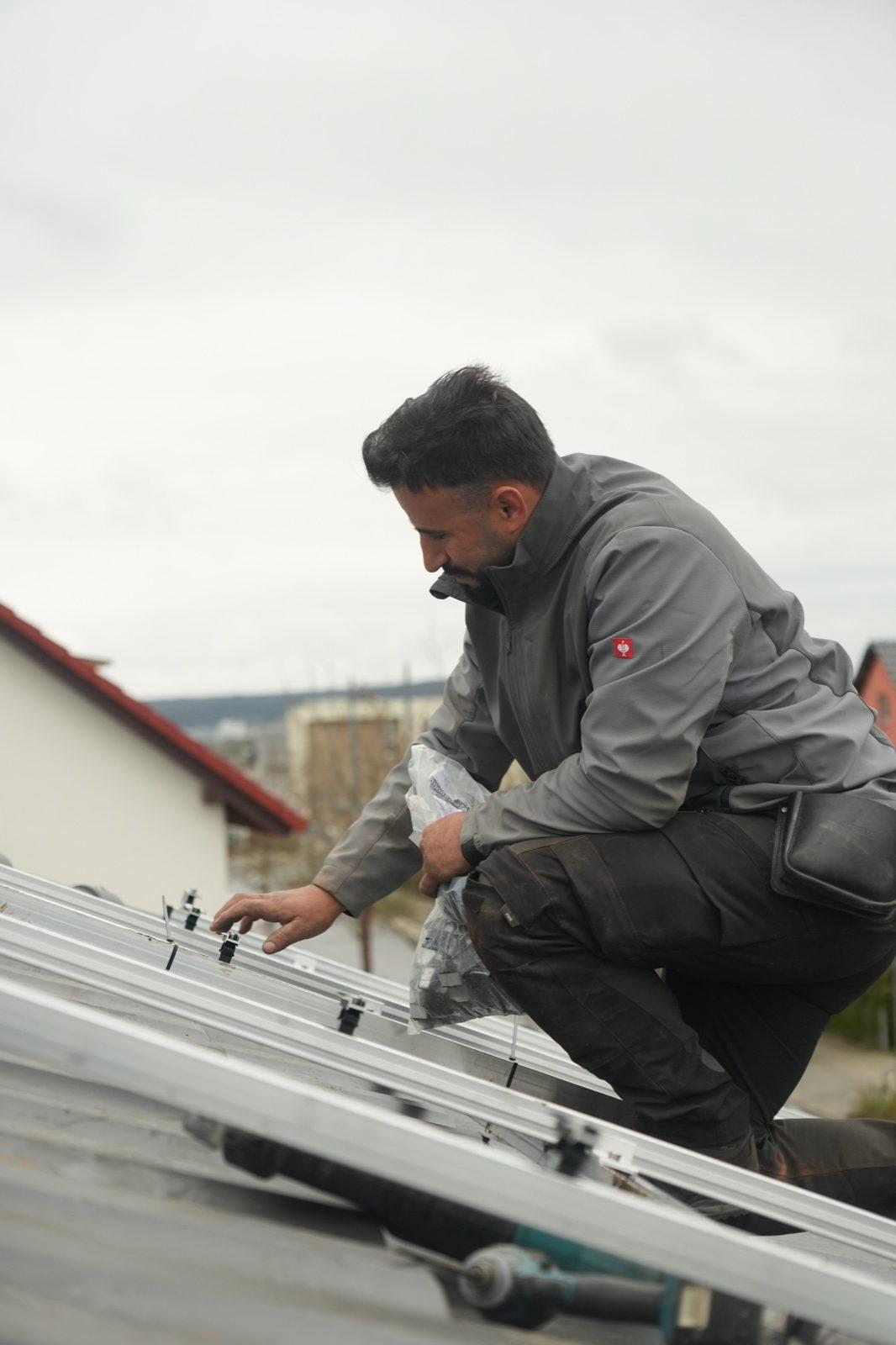 Monteur trägt ein Solarmodul über ein Ziegeldach