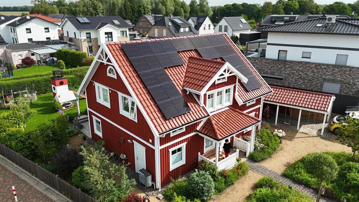 Rotes Schwedenhaus mit vollflächig belegtem Photovoltaikdach aus der Luft